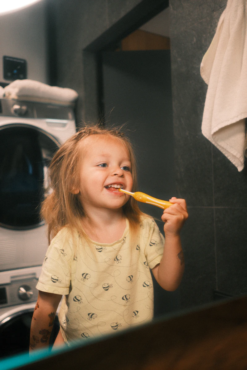 A small child smiling while brushing her teeth at home